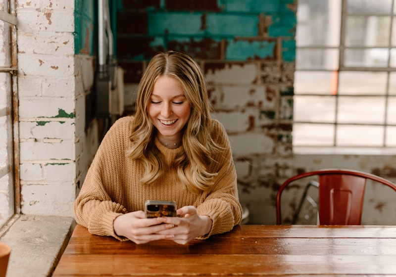 Mujer sonriendo mientras escribe en su teléfono, con luz cálida